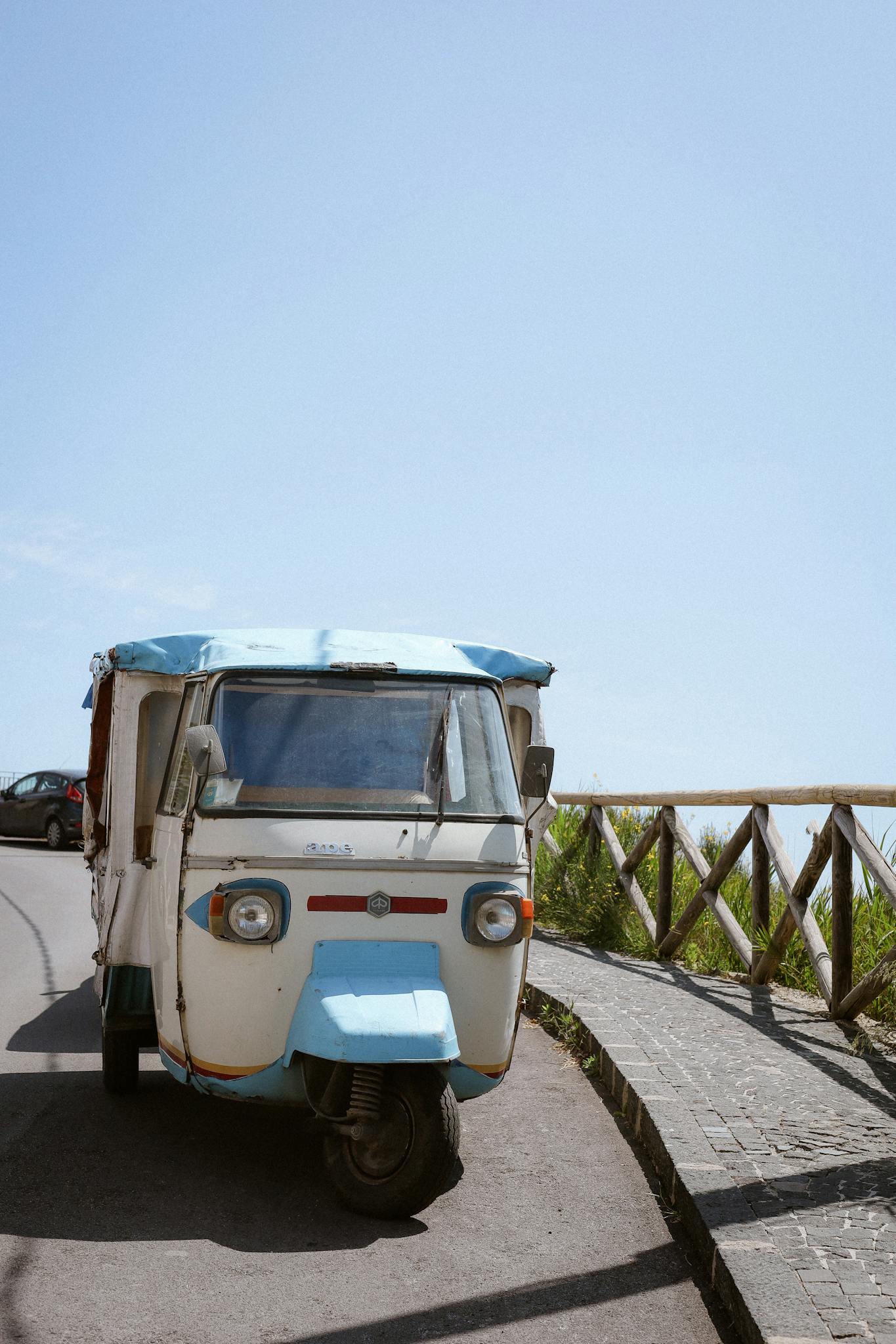 A classic Tuk Tuk parked on a sunny street with clear blue skies.