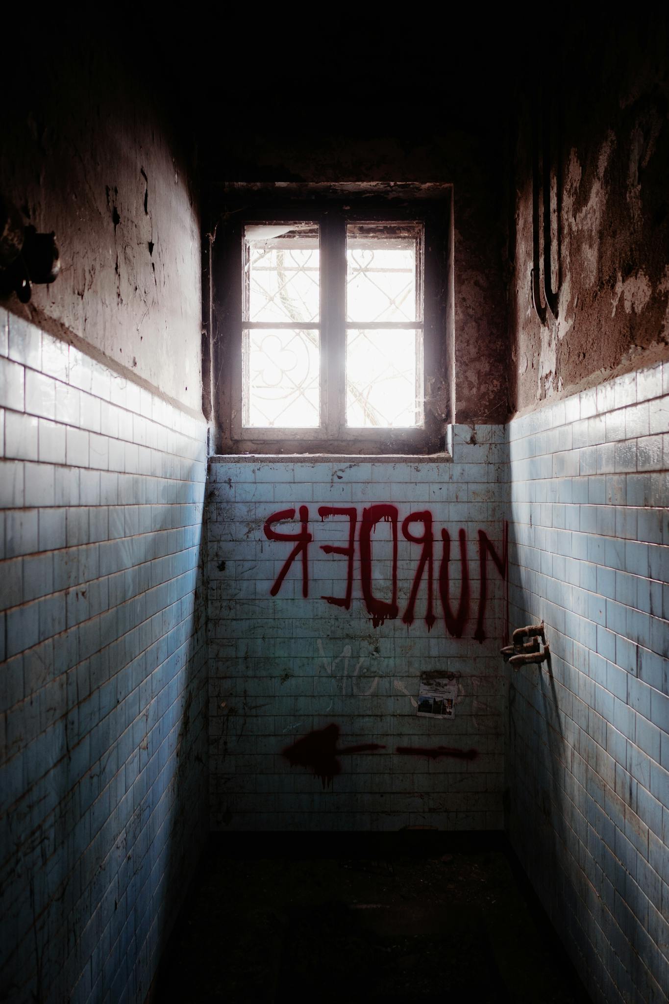 Abandoned hallway featuring red graffiti and a single window casting shadowy light.