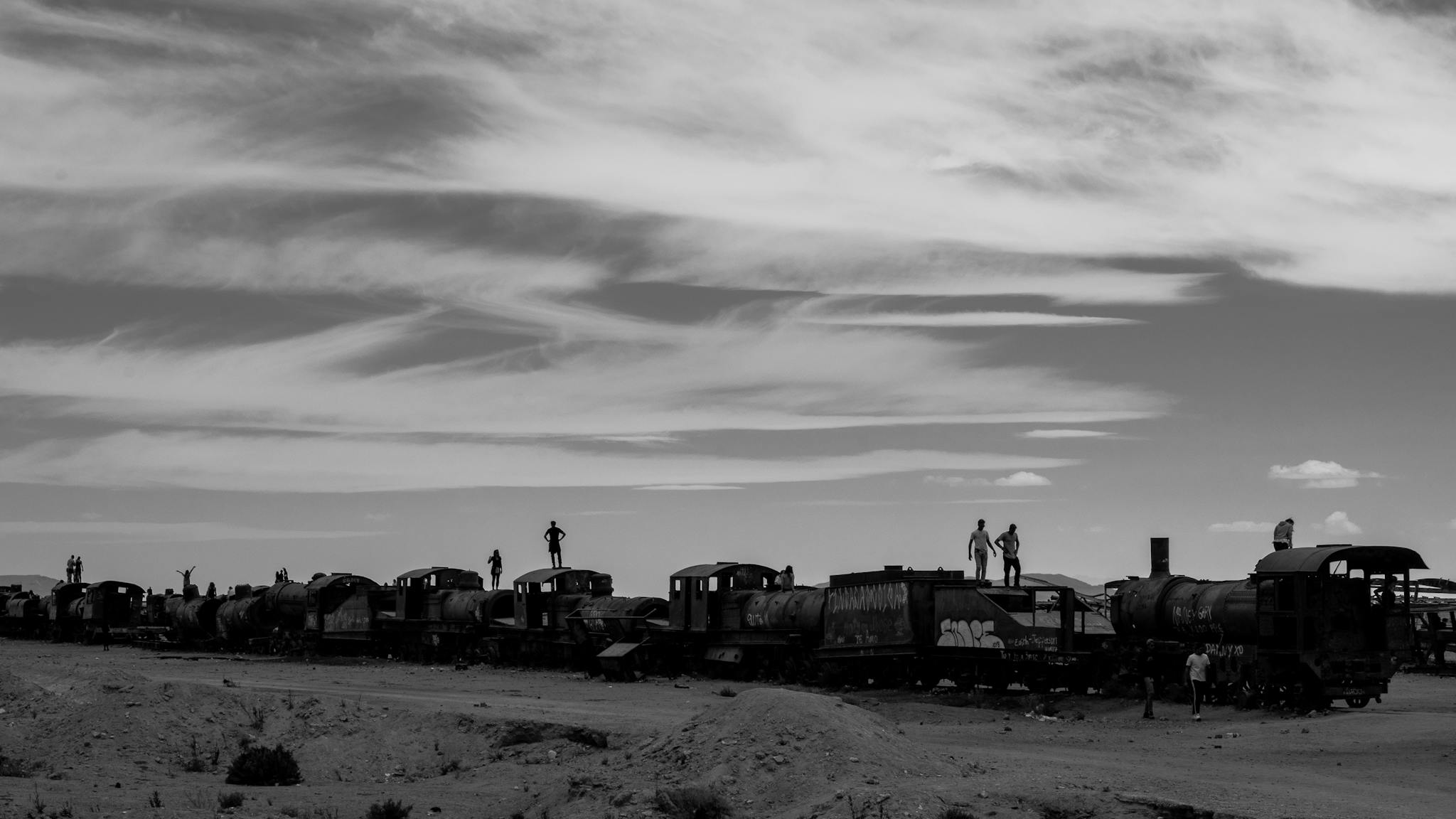 Black and white photo of people on abandoned trains in Bolivia's desert landscape.